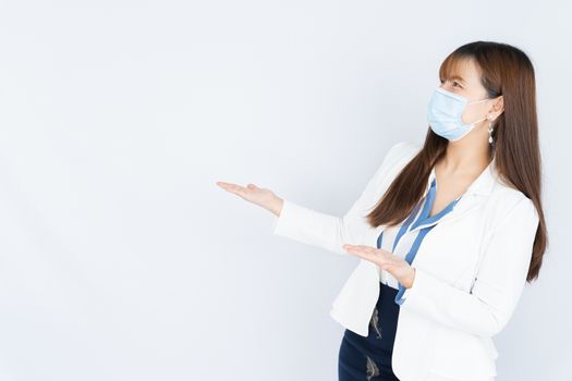 Smiling Asian business woman wearing a medical face mask and pointing hand to side blank space over grey background. Back to the normal concept.