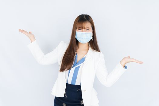 Smiling Asian business woman wearing a medical face mask and pointing hand to side blank space over grey background. Back to the normal concept.