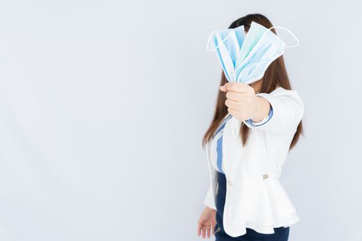 Business woman shows hand grasping mask over grey background. Back to the normal concept.