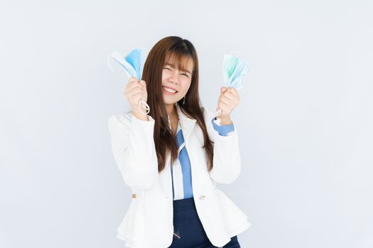 Smiling Asian business woman shows hand grasping mask over grey background. Back to the normal concept.