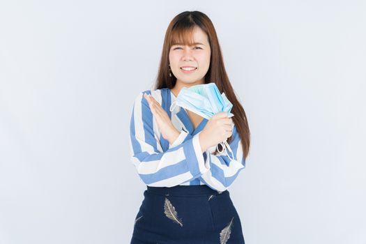 Smiling Asian business woman shows hand grasping mask and no hand sign to the mask over grey background. Back to the normal concept.