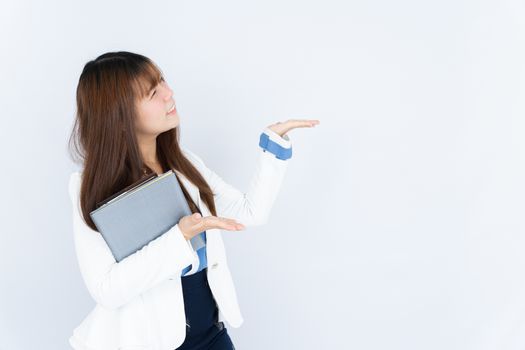 Smiling Asian business woman holding the notebook and pointing hand to side blank space over grey background. Back to the normal concept.