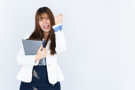 Smiling Asian business woman wearing a medical face mask holding the notebook and showing fist fighting over grey background. Back to the normal concept.