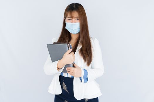 Smiling Asian business woman holding the notebook and looking at the camera over grey background. Back to the normal concept.