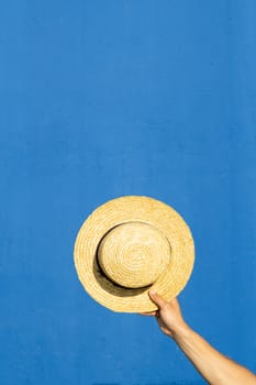 A man's hand holding a straw hat on a blue background. Summer, vacation concept.