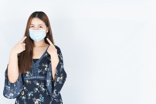 Asian beautiful happy hipster woman wearing a medical protection face mask for protect the coronavirus, filter dust PM 2.5 and cold and her finger point on her mask on white background