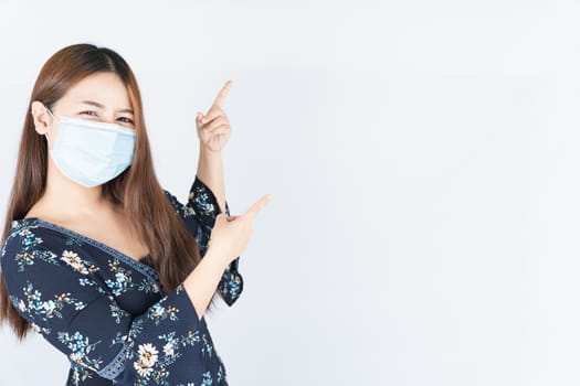 Asian beautiful happy hipster woman wearing a medical protection face mask for protect the coronavirus, filter dust PM 2.5 and cold and her finger pointing outside on the white background