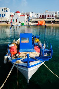 Blue fishing boat in port harbor of Chora town on Mykonos island with orthodox church in background, Greece