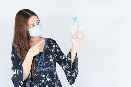 Asian beautiful happy hipster woman wearing a medical protection face mask for protect the coronavirus, filter dust PM 2.5 and cold and finger pointing to sanitizer hand gel on white background