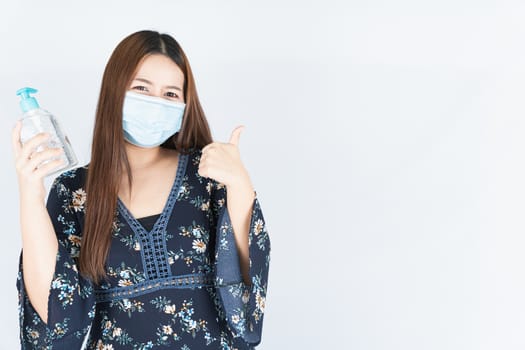 Asian beautiful happy hipster woman wearing a medical protection face mask for protect the coronavirus, filter dust PM 2.5 and cold and showing sanitizer hand gel and thumbs up on white background