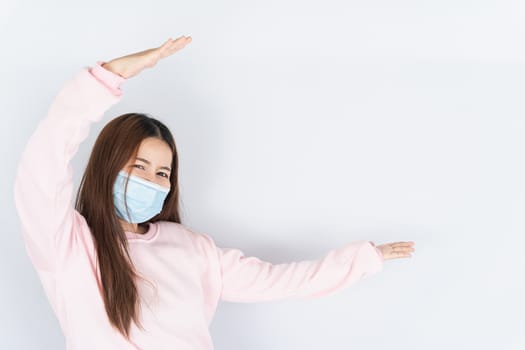 Asian beautiful happy hipster woman wearing a medical protection face mask for protect the coronavirus, filter dust PM 2.5 and cold and her finger pointing outside on the white background