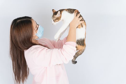 Asian beautiful happy woman wearing a medical protection face mask for protect the coronavirus, filter dust PM 2.5, cold and allergic to cat fur and she carry a cat on the white background