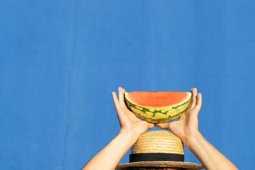 Young man in hat holding a piece of watermelon above his head. Summer, diet and weight loss concept.
