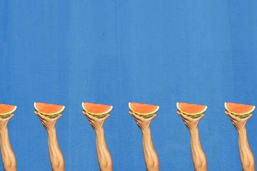 Man's arm holding a piece of watermelon on a blue background. Summer concept, slimming, summer