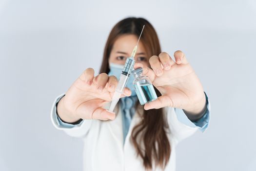 Closeup hand of woman doctor or scientist wearing medical mask and holding medicine liquid vaccine vial bottle. COVID 19 or coronavirus concept.