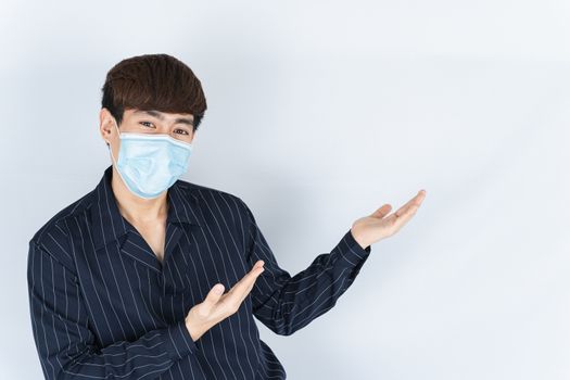 Asian handsome happy hipster man wearing a medical protection face mask for protect the coronavirus, filter dust PM 2.5 and cold and her finger pointing outside on the white background