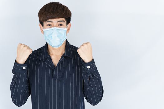 Asian handsome happy hipster man wearing a medical protection face mask for protect the coronavirus, filter dust PM 2.5 and cold and raise her hand to fight them on white background