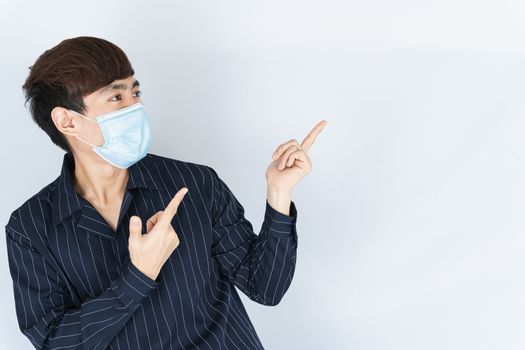 Asian handsome happy hipster man wearing a medical protection face mask for protect the coronavirus, filter dust PM 2.5 and cold and her finger pointing outside on the white background