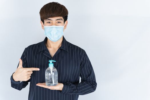 Asian handsome happy hipster man wearing a medical protection face mask for protect the coronavirus, filter dust PM 2.5 and cold and finger pointing to sanitizer hand gel on white background