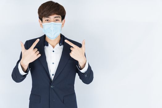 Asian handsome happy business man wearing a medical protection face mask for protect the coronavirus, filter dust PM 2.5 and cold and her finger point on her mask on white background