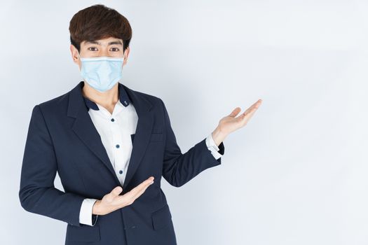 Asian handsome happy business man wearing a medical protection face mask for protect the coronavirus, filter dust PM 2.5 and cold and her finger pointing outside on the white background