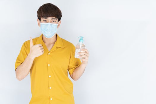 Asian handsome happy hipster man wearing a medical protection face mask for protect the coronavirus, filter dust PM 2.5 and cold and showing sanitizer hand gel and thumbs up on white background