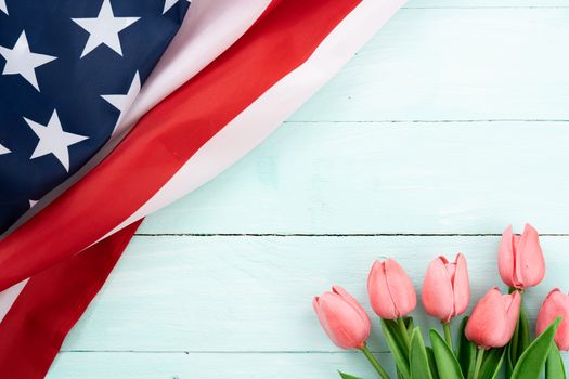 US American flag with tulip flower on blue wooden background. For USA Memorial day,  Presidents day, Veterans day, Labor day, Independence or 4th of July celebration. Top view, copy space for text.