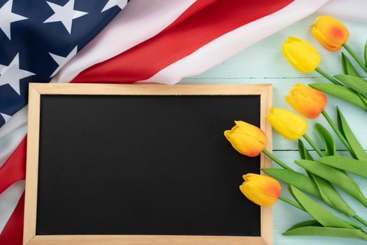 US American flag with blackboard and tulip flower on blue wooden background. For USA Memorial day, Presidents day, Veterans day, Labor day, Independence or 4th of July celebration. Top view, copy space for text.