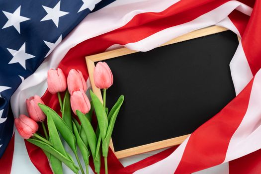 US American flag with blackboard and tulip flower on blue wooden background. For USA Memorial day, Presidents day, Veterans day, Labor day, Independence or 4th of July celebration. Top view, copy space for text.