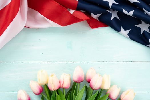 US American flag with tulip flower on blue wooden background. For USA Memorial day,  Presidents day, Veterans day, Labor day, Independence or 4th of July celebration. Top view, copy space for text.