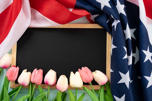 US American flag with blackboard and tulip flower on blue wooden background. For USA Memorial day, Presidents day, Veterans day, Labor day, Independence or 4th of July celebration. Top view, copy space for text.