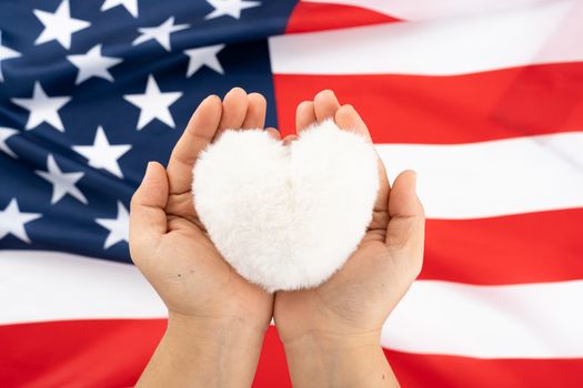 US American flag with hand holding white heart shape on white background. For USA Memorial day, Presidents day, Veterans day, Labor day, Independence or 4th of July celebration. Top view, copy space for text.