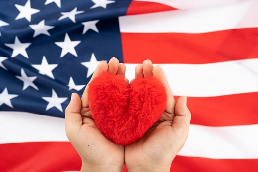 US American flag with hand holding red heart shape on white background. For USA Memorial day, Presidents day, Veterans day, Labor day, Independence or 4th of July celebration. Top view, copy space for text.