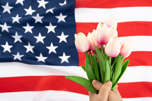 US American flag with hand holding tulip flower on white background. For USA Memorial day, Presidents day, Veterans day, Labor day, Independence or 4th of July celebration. Top view, copy space for text.