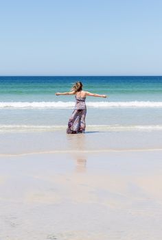 Middle-aged blonde woman relaxing at the beach with arms open enjoying her freedom facing the sea