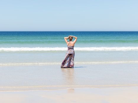Woman relaxing on the beach with her hands on the back of her head enjoying her freedom facing the sea