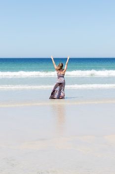 Middle-aged blonde woman relaxing at the beach with arms open enjoying her freedom facing the sea