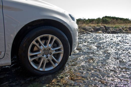 White off-road vehicle drives over water of a river in the mountains of Norway.