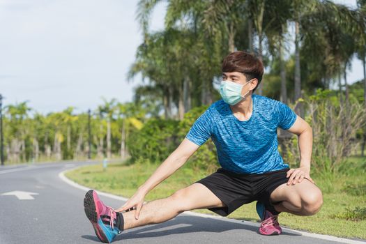 Young male wearing medical mask and stretching his legs before workout training session at the park. Stay in fit during quarantine in the days of the Corona Virus or Covid-19