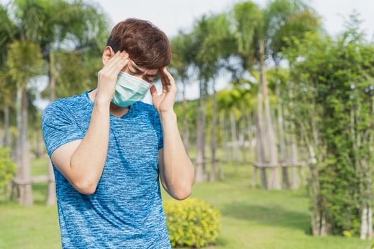 Young male wearing medical mask have headache while workout at the park. Stay in fit during quarantine in the days of the Corona Virus or Covid-19