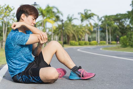 Asian man use hands hold on his elbow while running on road in the park. Injury from workout concept.