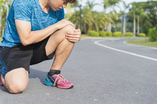 Asian man use hands hold on his knee injury while running on road in the park, Injury from workout concept.