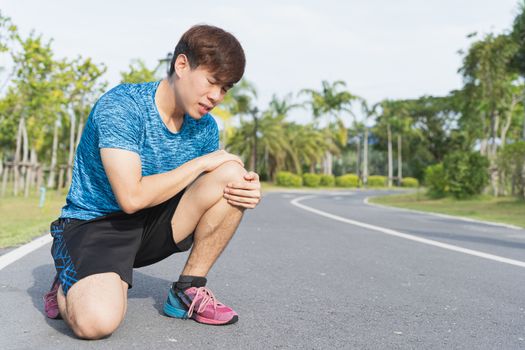 Asian man use hands hold on his knee injury while running on road in the park, Injury from workout concept.