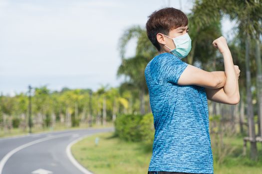 Young male wearing medical mask and stretching his arms before workout training session at the park. Stay in fit during quarantine in the days of the Corona Virus or Covid-19