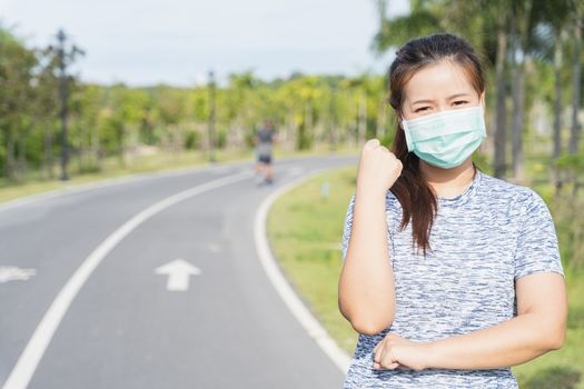 Young female wearing medical mask and show her hand to fight them before workout training session at the park. Stay in fit during quarantine in the days of the Corona Virus or Covid-19