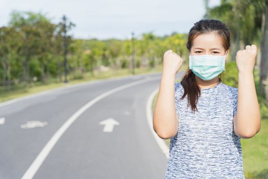 Young female wearing medical mask and show her hand to fight them before workout training session at the park. Stay in fit during quarantine in the days of the Corona Virus or Covid-19