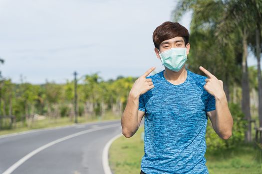 Young male pointing at the medical mask before workout training session at the park. Stay in fit during quarantine in the days of the Corona Virus or Covid-19