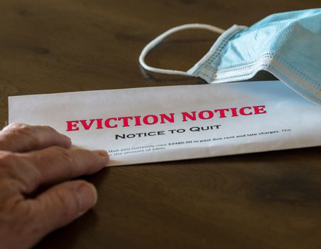 Defaulting renter with facemask receives letter giving notice of eviction from home on wooden table