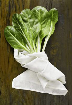  Leaves of chard -Swiss chard - on wooden table , several green leaves with white stalks  covered with white cotton cloth 