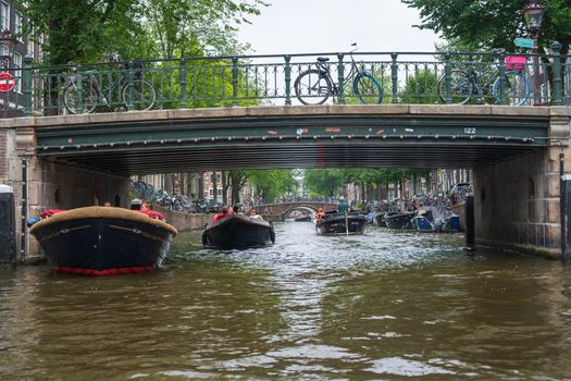 Amsterdam, the Netherlands — July 28, 2019. Photo looking under a bridge of boats traveling on one of Amsterdam's canals.